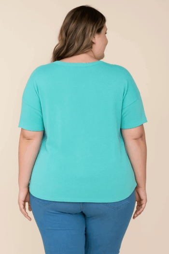 Back view of a mid-size woman wearing a seafoam knit short sleeve top with a smooth, straight back and relaxed fit, shown on a studio background.