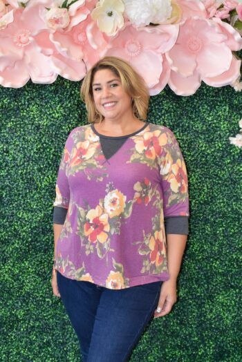 Front view of a plus-size model wearing the Saturday Hacci Floral Top in a vibrant plum base with bold floral prints, lightweight hacci knit fabric, and a casual-chic fit — perfect for effortless weekend style.