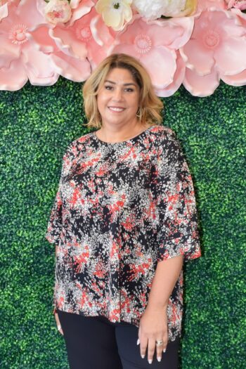 Plus size woman wearing Dear Scarlett berry print flutter sleeve top with black, red, and berry tones – styled with brown slim pants.