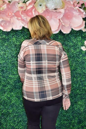 Back view of a plus size woman wearing a brown and black plaid long sleeve top, standing in front of a floral green wall at Botticelli Boutique.