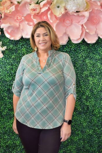 Plus size woman wearing a sage green plaid 3/4 sleeve top with roll-tab sleeves and split neckline, front view, styled with black pants at Botticelli Rhode Island.