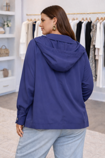 Back view of a woman wearing a lightweight Easy A-Line hooded jacket, showing the relaxed drape, attached hood, and clean silhouette in a boutique setting.