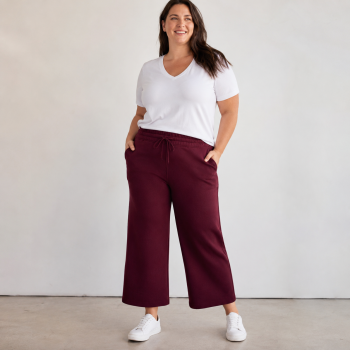 Mid-size woman wearing burgundy Cropped Wide Leg Scuba Pants with a relaxed high-rise fit, wide-leg silhouette, and white V-neck tee.